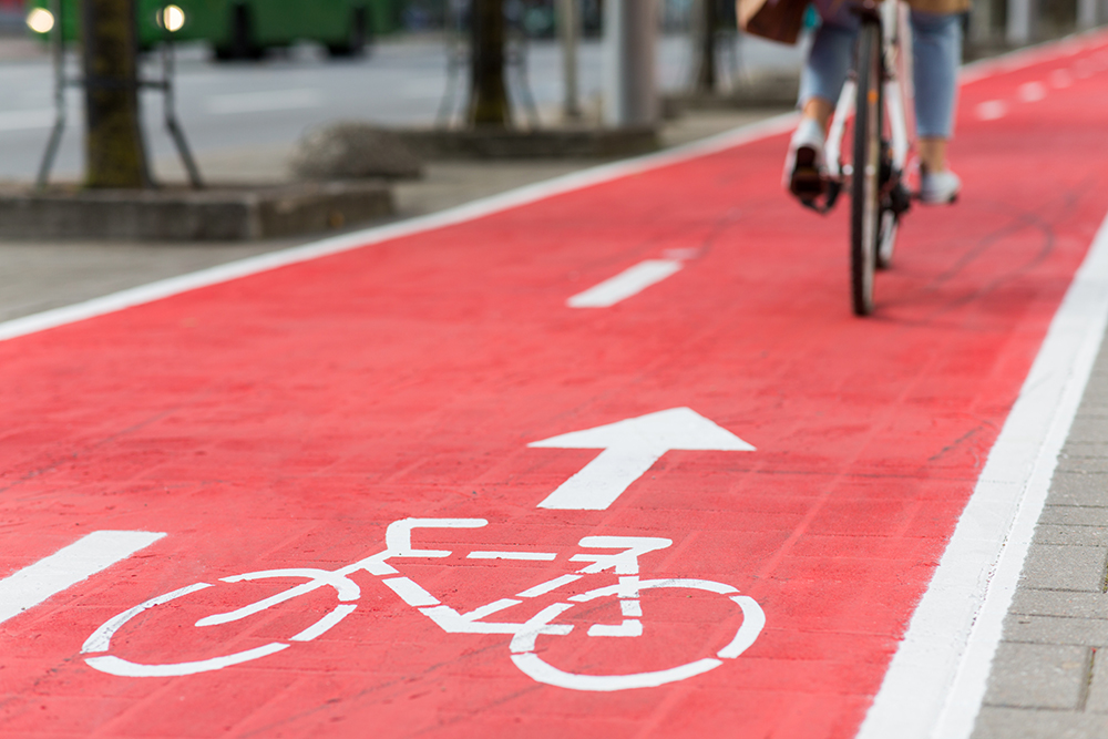 traffic, city transport and people concept - woman cycling along red bike lane with signs of bicycles on street